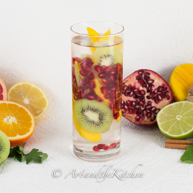 tall glass of water with kiwi, pomegranate, and mango slices.