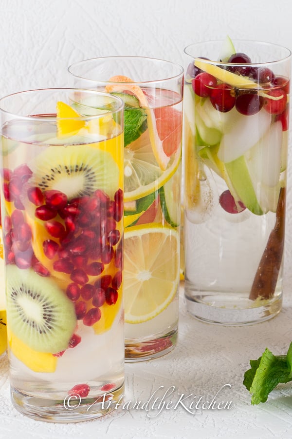 Three tall glasses filled with water and fresh fruit.