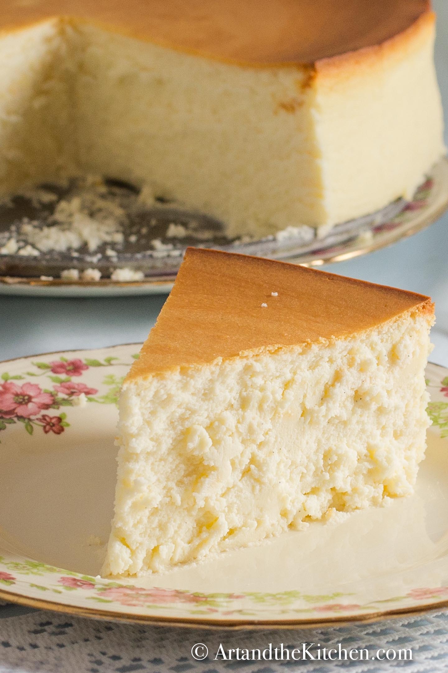 Slice of plain crustless cheesecake on decorative plate with whole cheesecake in background.