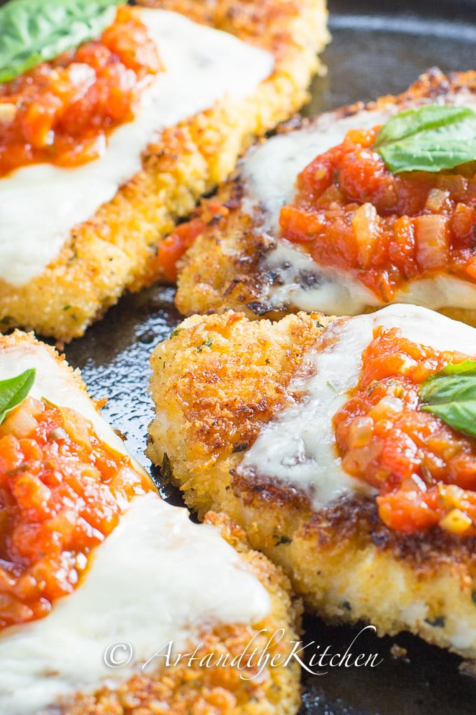 Four pieces of chicken parmesan served in cast iron skillet topped with marinara sauce and a basil leaf.