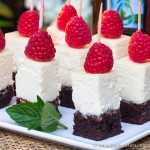 Bite size pieces of cheesecake with brownie crust topped with a raspberry held with wood toothpick