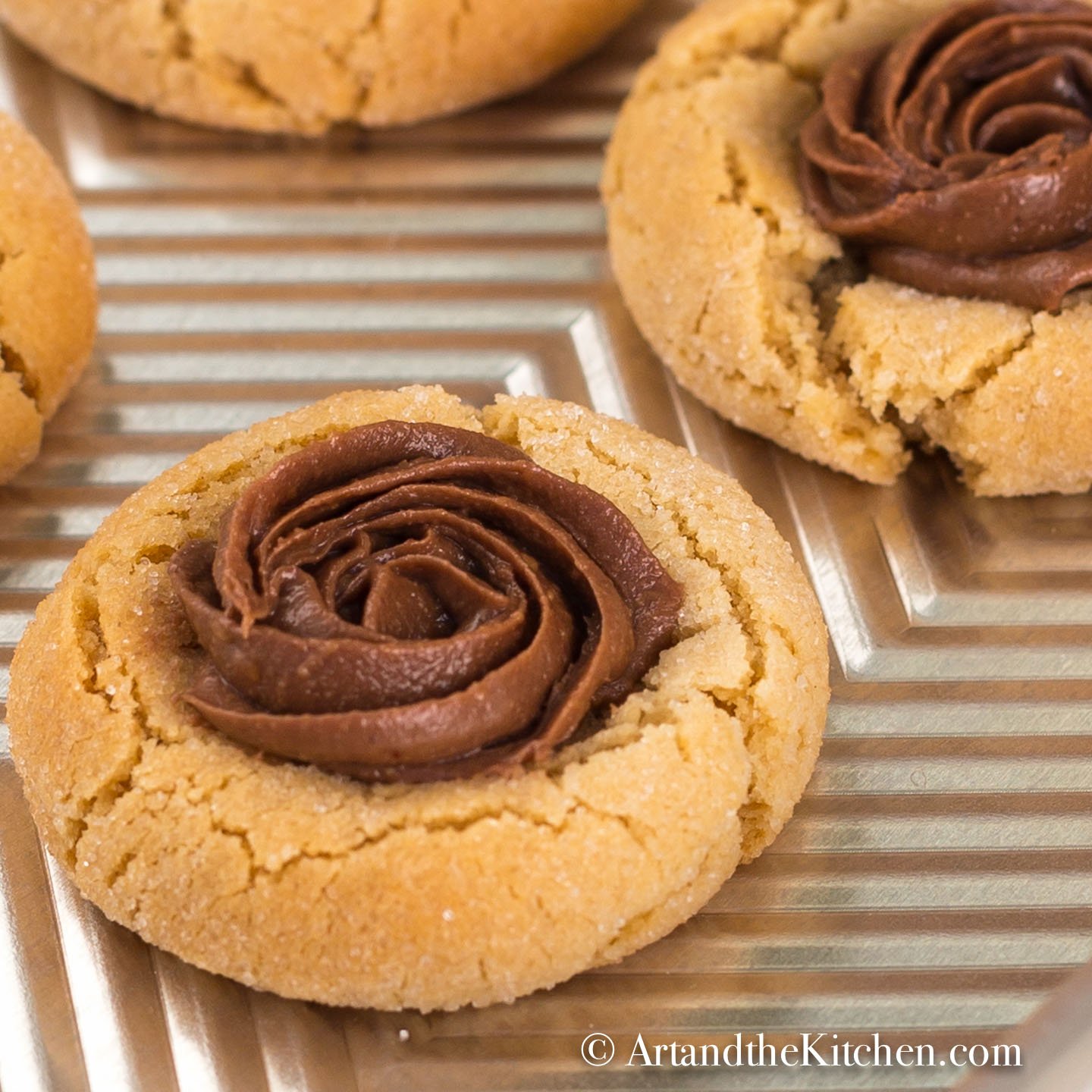 A baking sheet filled with peanut butter cookies topped with swirl of whipped chocolate.