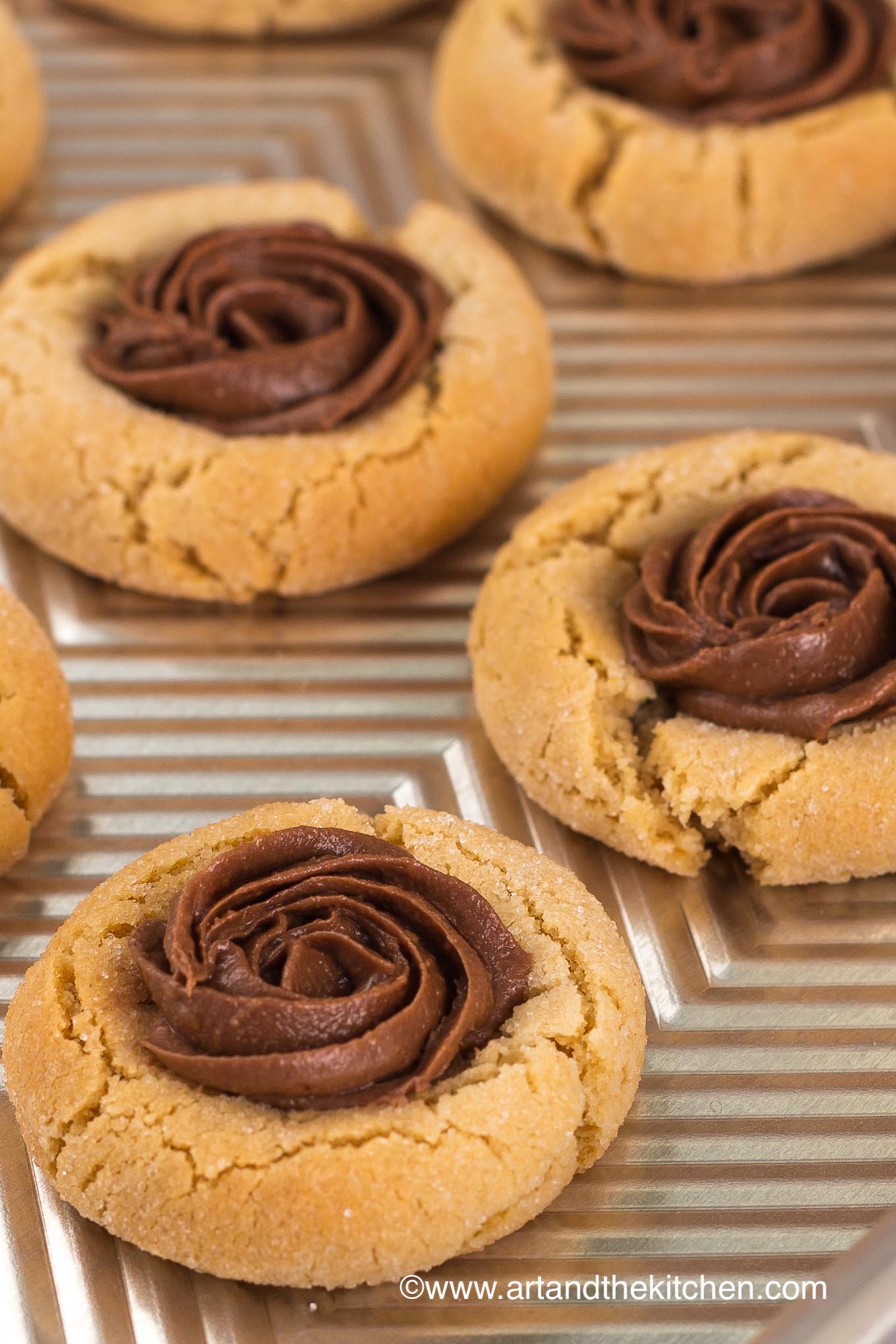 A baking sheet filled with peanut butter cookies topped with a dollop of whipped chocolate.