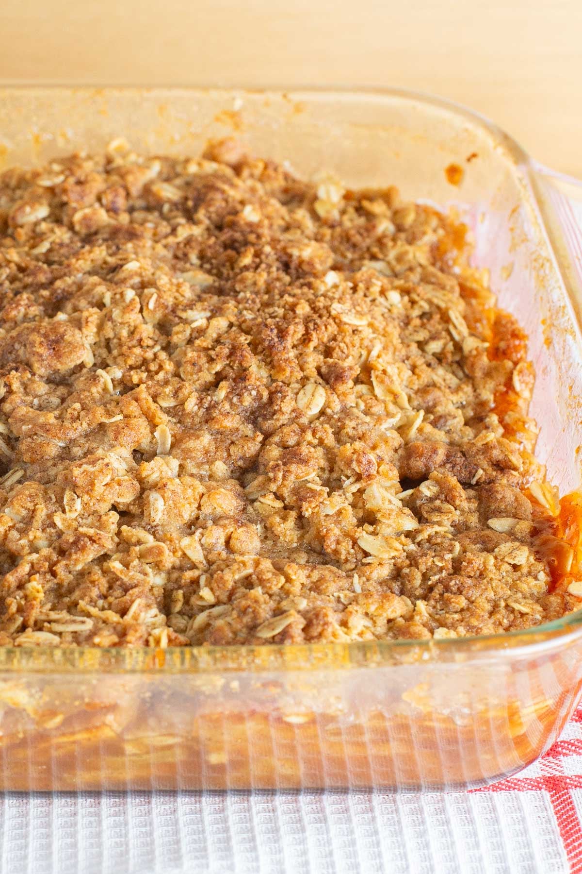 Glass baking dish filled with golden oat crumble topping over warm baked fruit, served on a red-and-white checkered tablecloth.