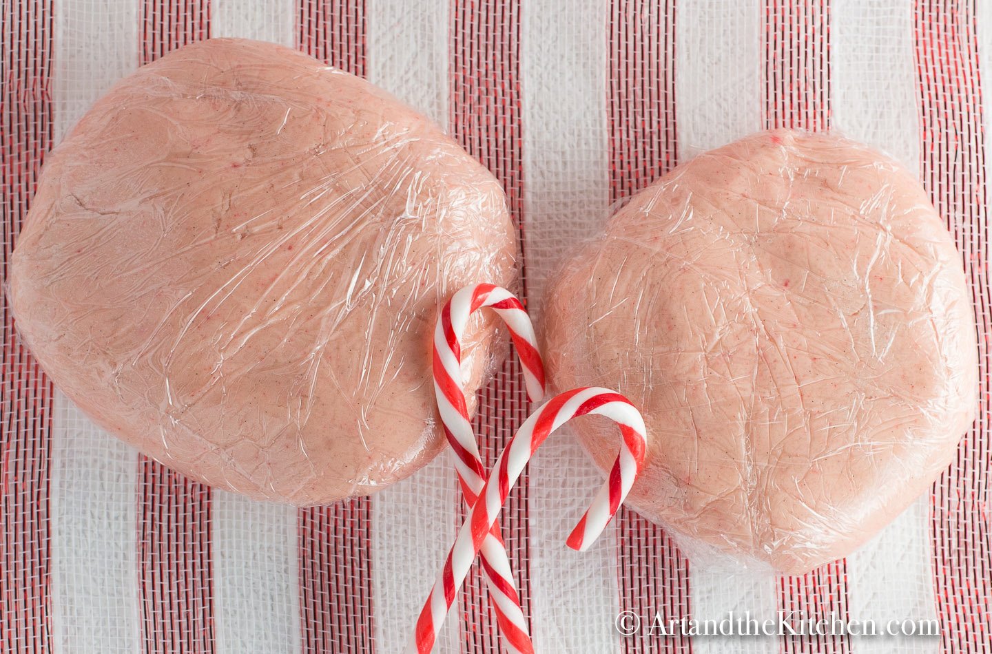 Two disks of pink candy cane flavored dough wrapped in plastic wrap. 