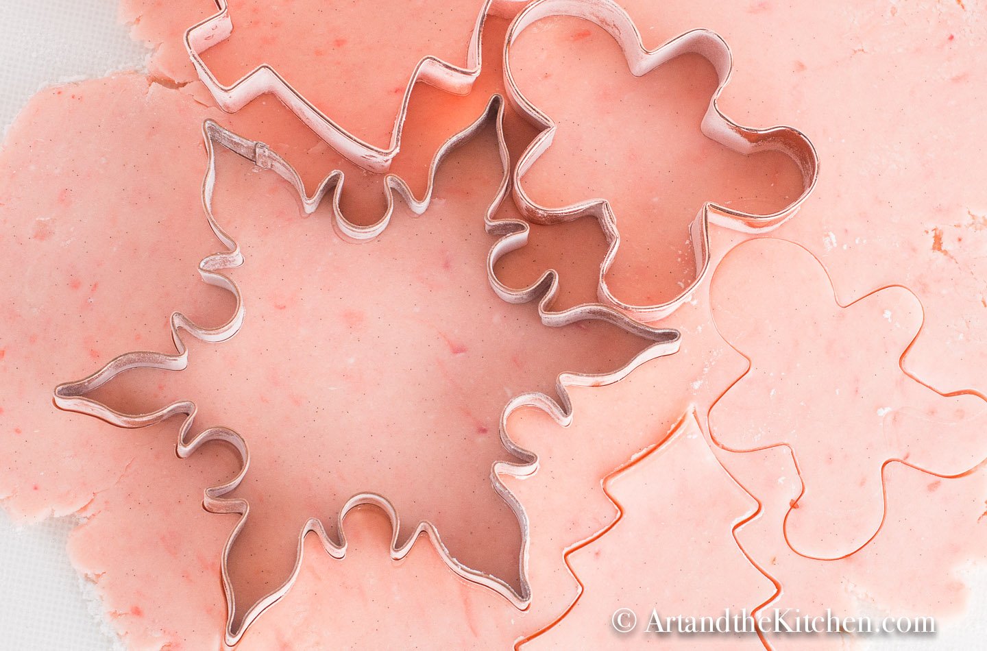 Pink sugar cookie dough rolled out with snowflake and gingerbread men cookie cutters.