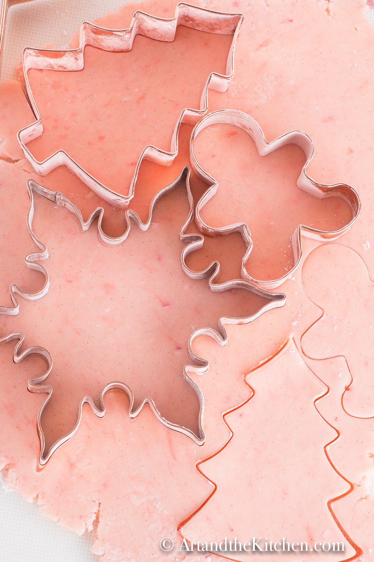 Pink tinted sugar cookie dough rolled out with copper Holiday shaped cookie cutters.