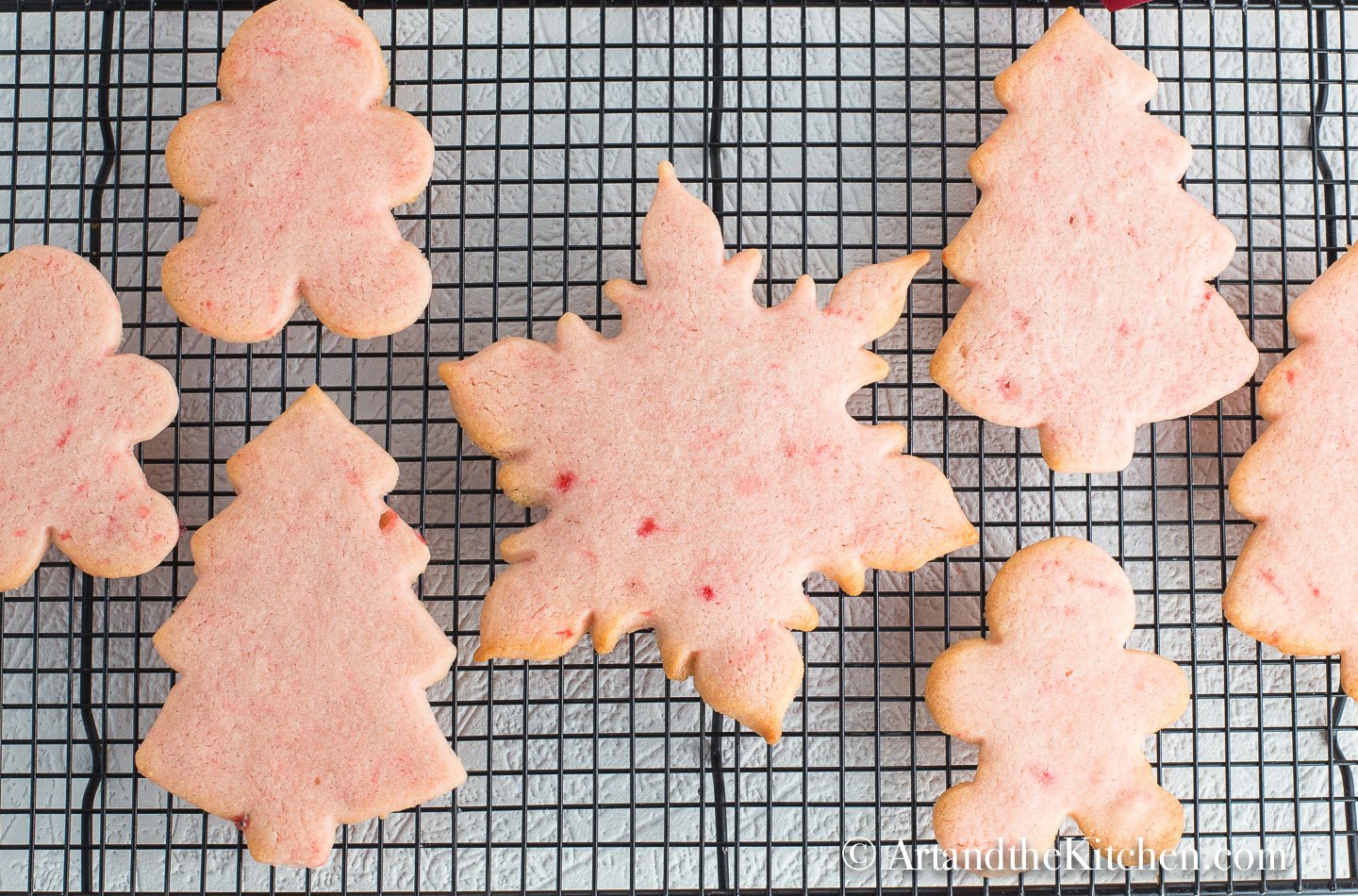 Pink colored cookies in Christmas cookie shapes cooling on cooling rack.
