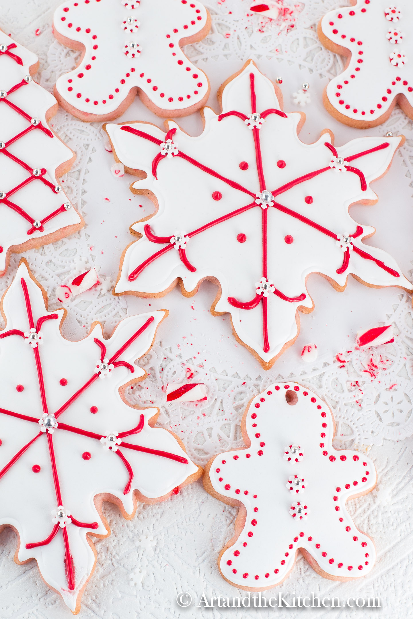 Sugar cookies cut into snowflake and gingerbread men shapes, coated with white royal icing and decorated with red dots and lines.