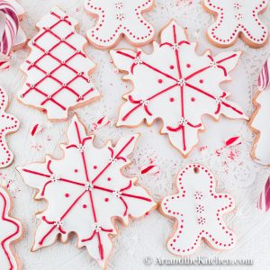 Sugar cookies cut into snowflake and gingerbread men shapes, coated with white royal icing and decorated with red dots and lines.