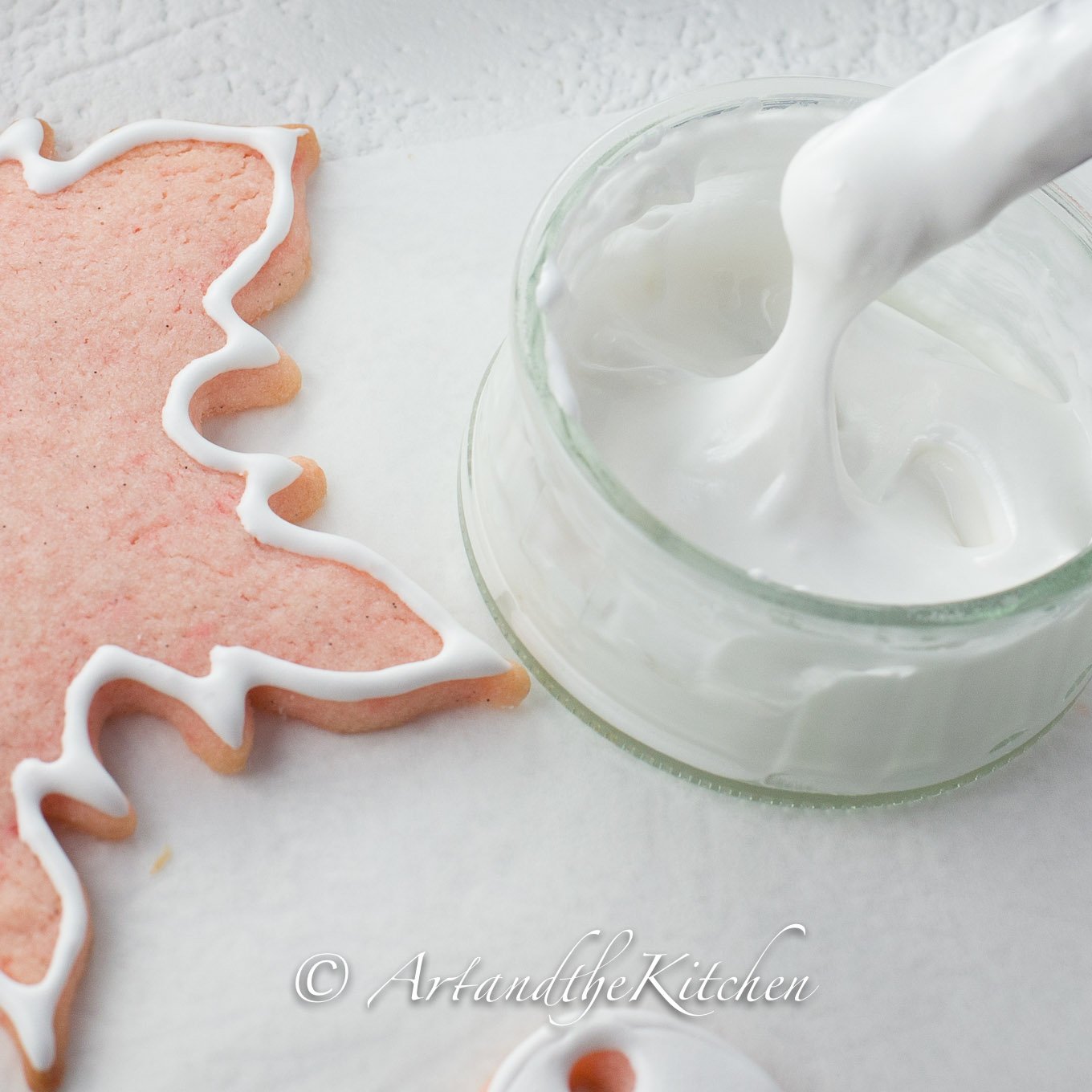 Small glass bowl filled with royal icing and pink snowflake cookie.