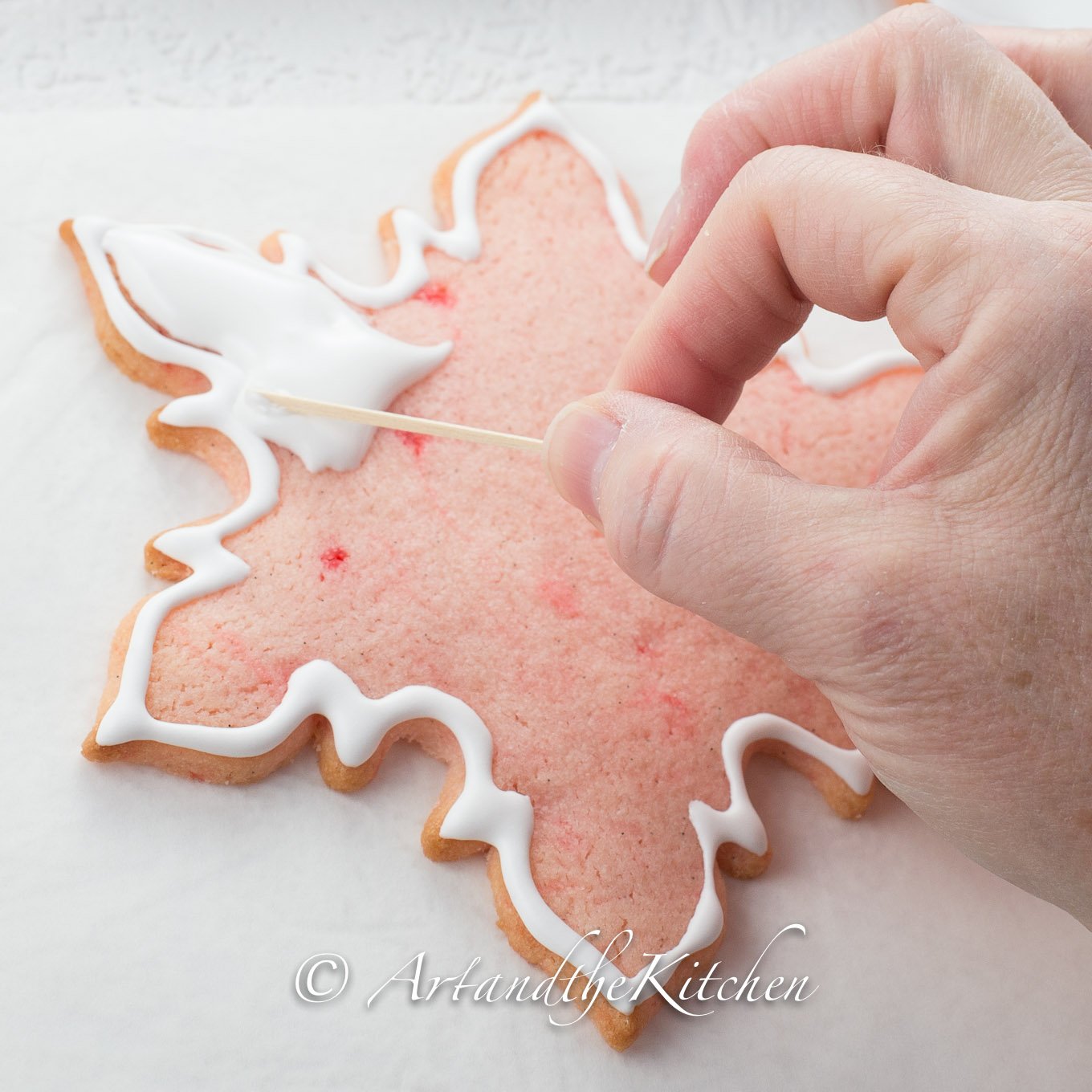 Pink snowflake cookie being decorated with royal icing.