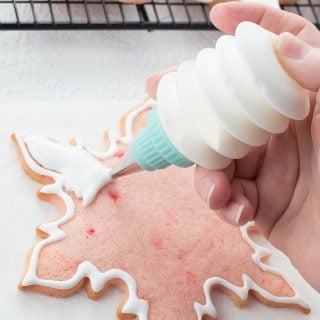 Pink snowflake shaped cookie being decorated with royal icing from squeeze bottle.