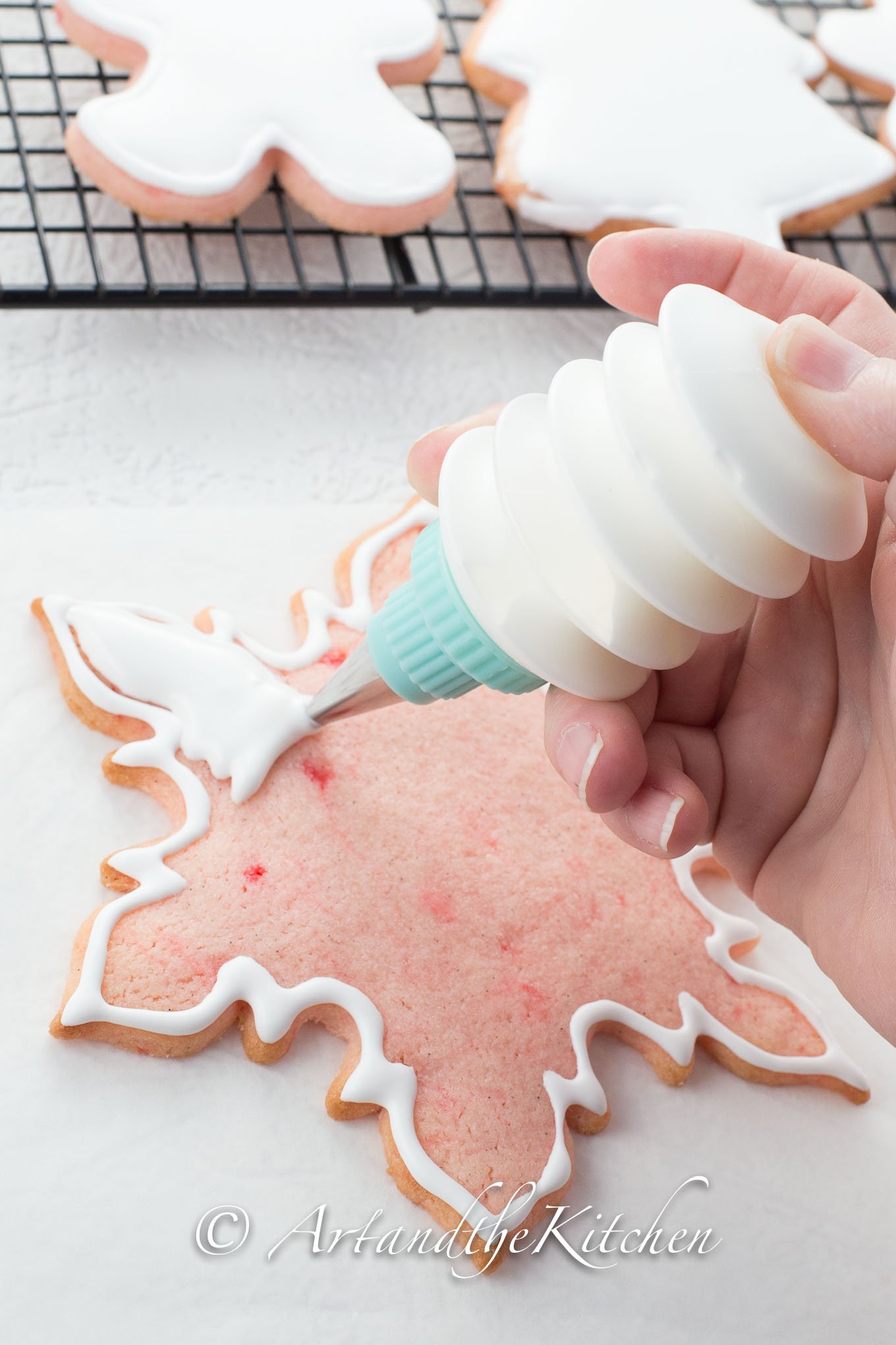 Pink snowflake shaped cookie being decorated with royal icing from squeeze bottle.