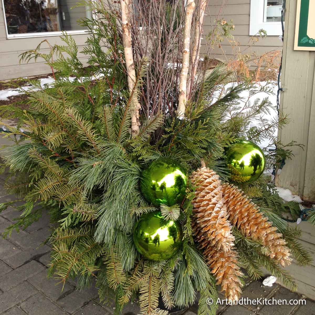 Outdoor Christmas planter with greenery, tree branches and decorations.