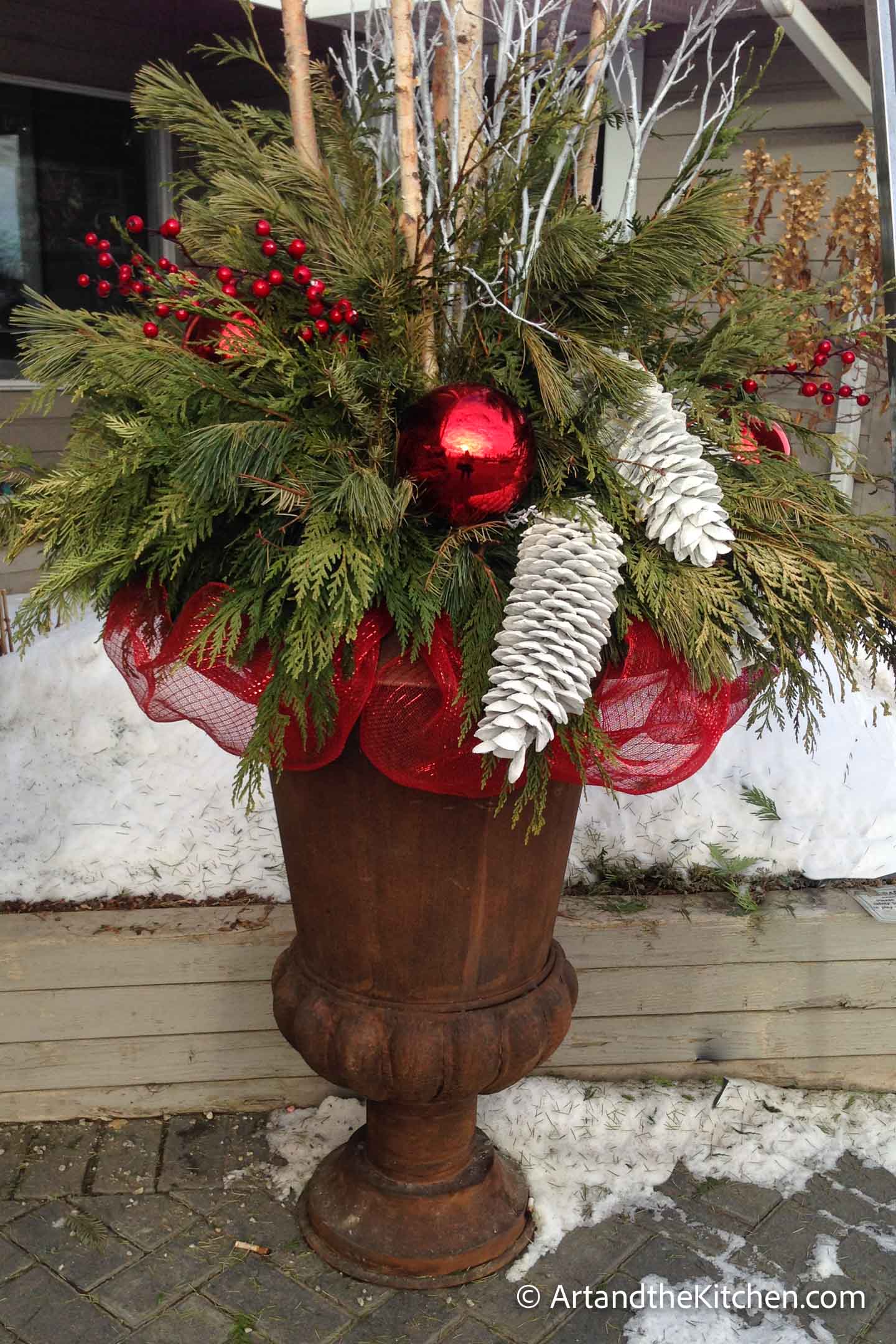 Outdoor Christmas planter with greenery, tree branches and decorations.