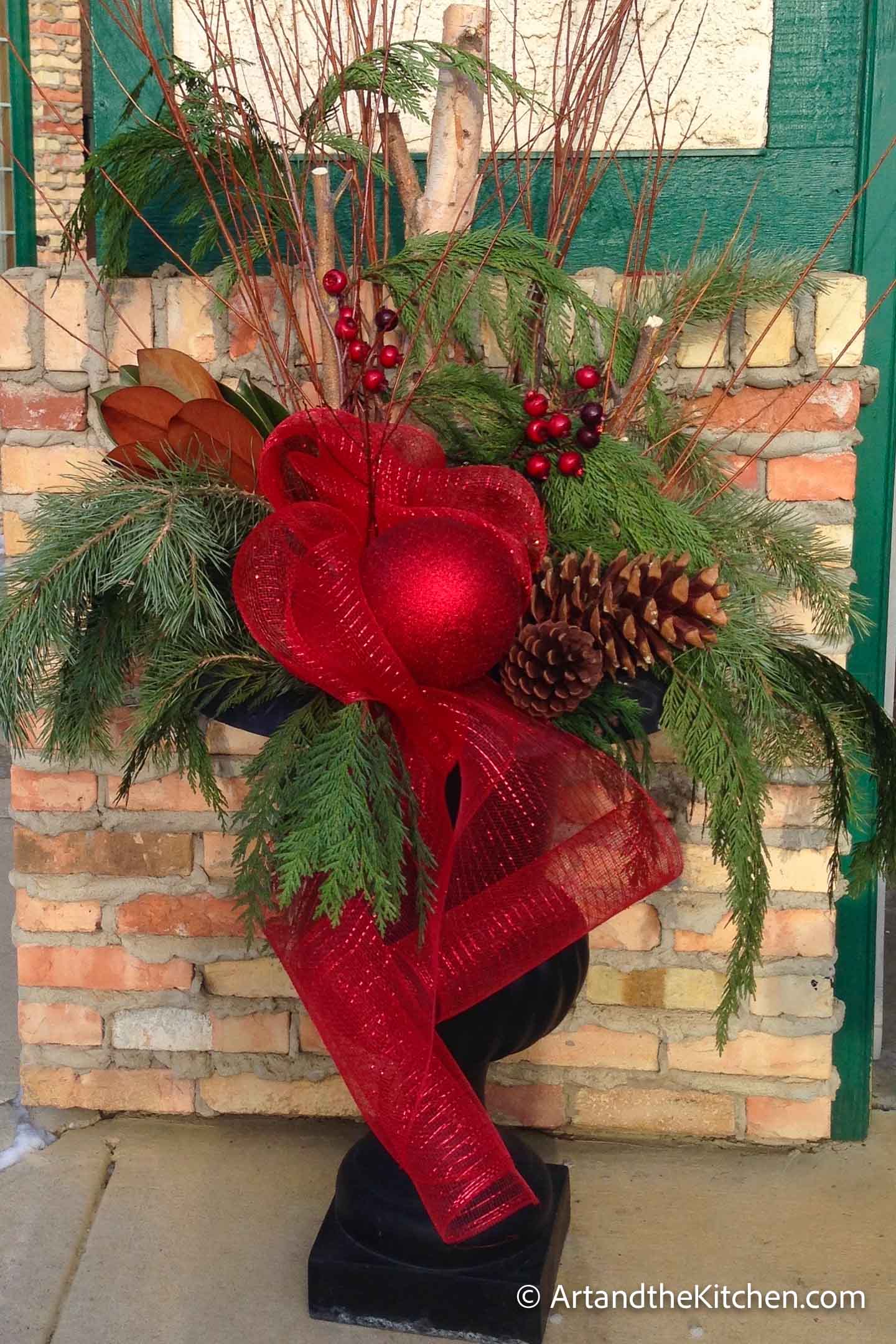 Outdoor Christmas planter with greenery, tree branches and decorations.