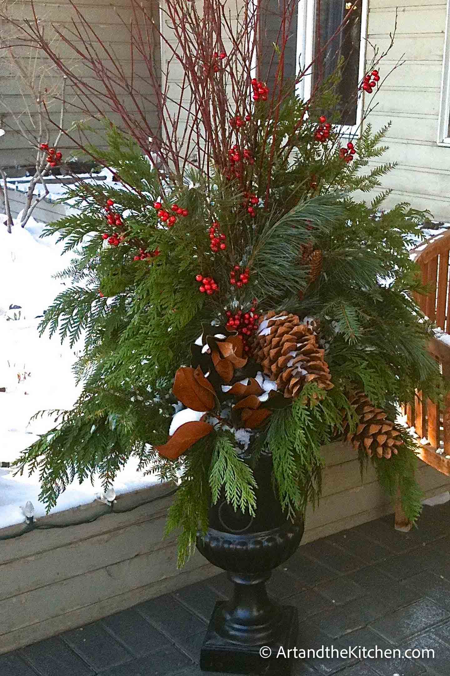 Outdoor Christmas planter with greenery, tree branches and decorations.