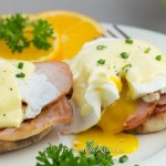 Eggs Benedict with ham, garnished with orange slices.