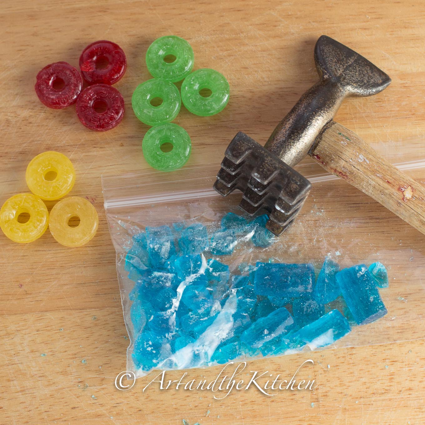 Colored hard candies and plastic bag filled with crushed blue candies with a meat mallet. 