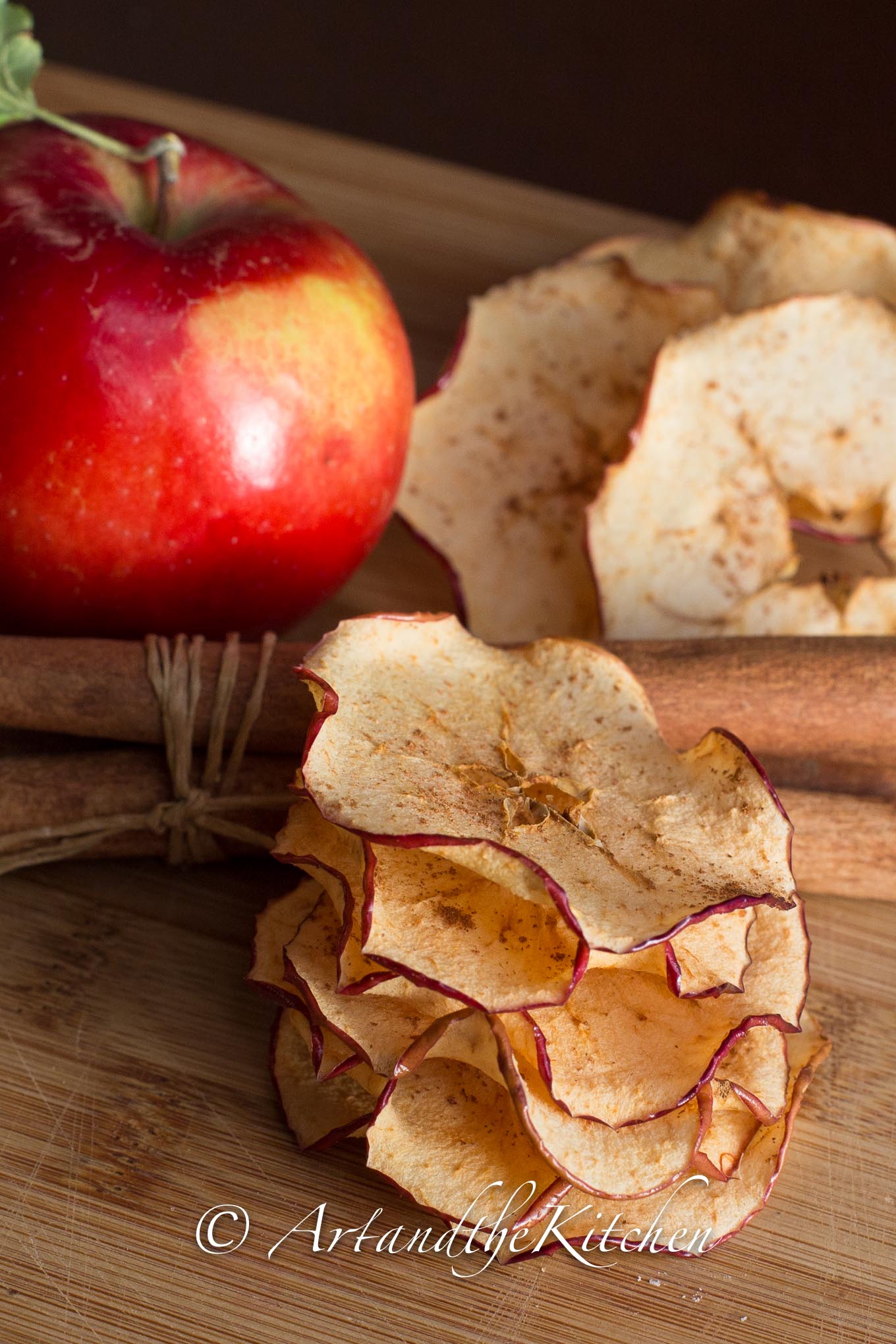 Stack of crisp apple chips with apple and cinnamon sticks.