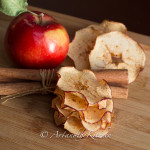 Stack of crisp apple chips with apple and cinnamon sticks.