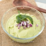 Avocado dip garnished with red onions, lime slice and cilantro in small glass bowl.