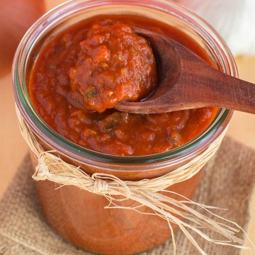Wooden spoon scooping enchilada sauce from glass jar filled with enchilada sauce.