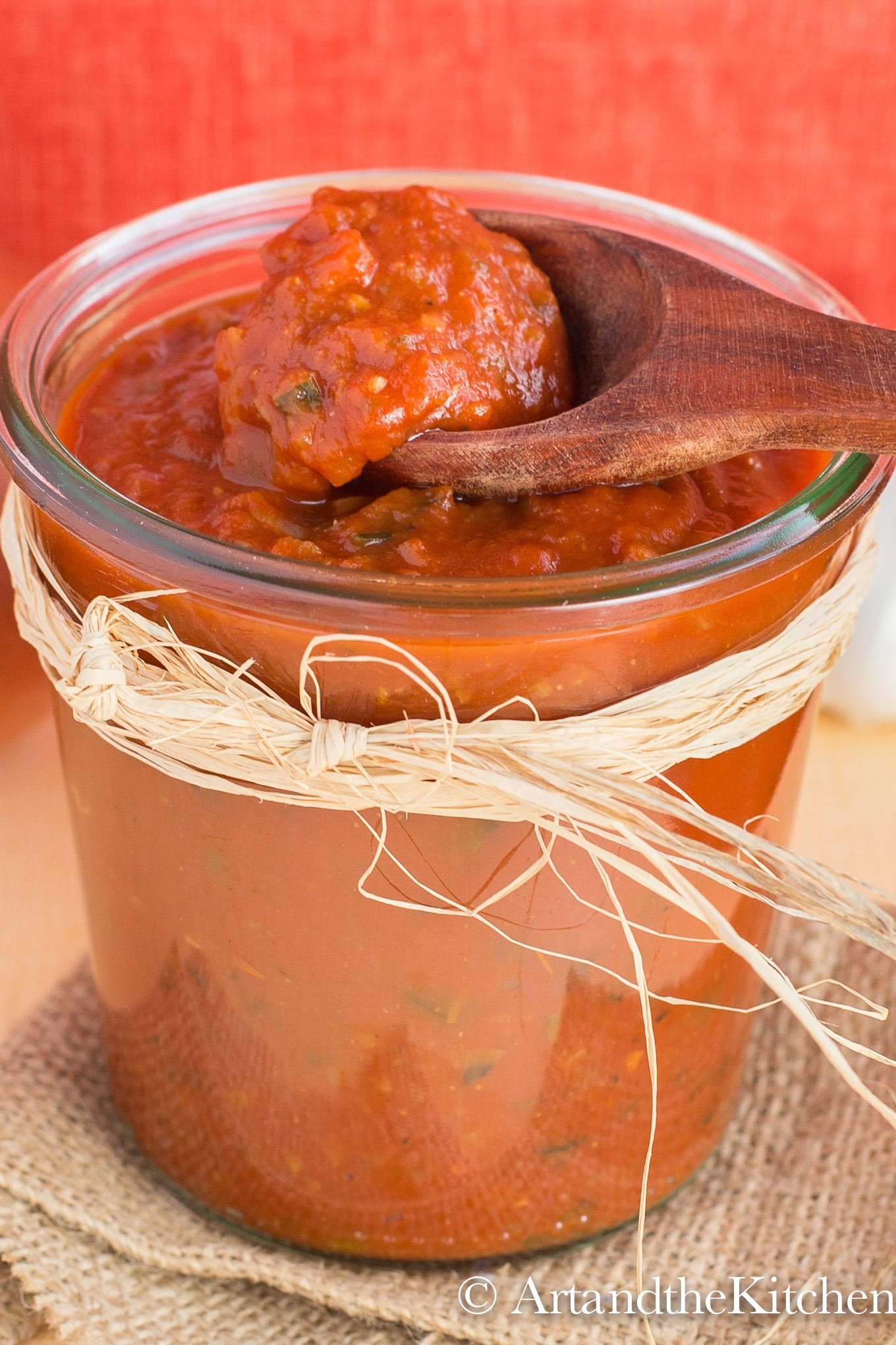 Wooden spoon scooping enchilada sauce from glass jar filled with enchilada sauce.