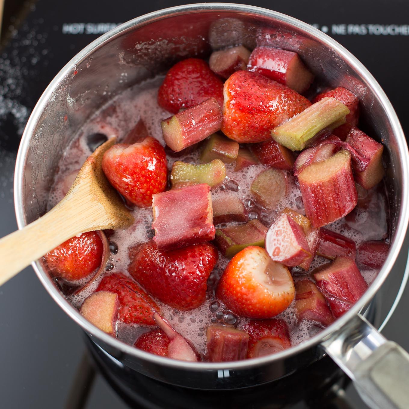 Rhubarb, strawberries and sugar cooking in stainless steel pot.