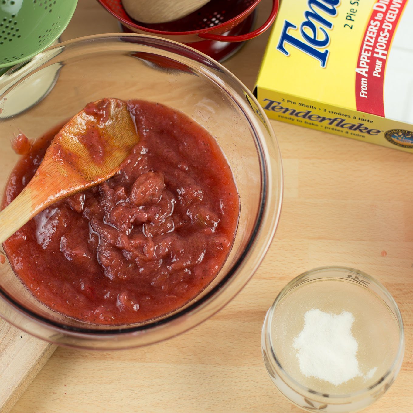 Strawberry rhubarb puree in glass bowl with wood spoon.