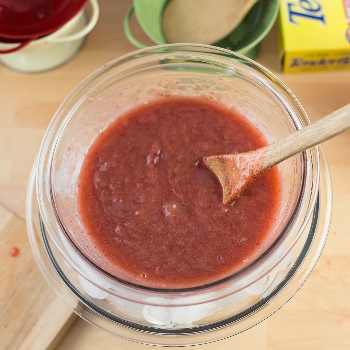 Strawberry rhubarb puree in glass bowl with wood spoon.