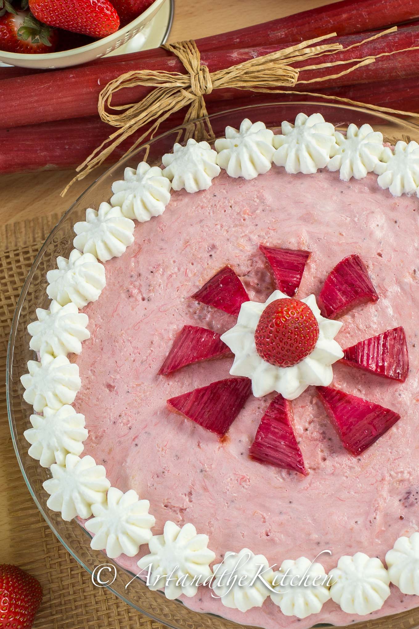 Mousse pie with strawberries and rhubarb, decorated with whipped cream dollops.