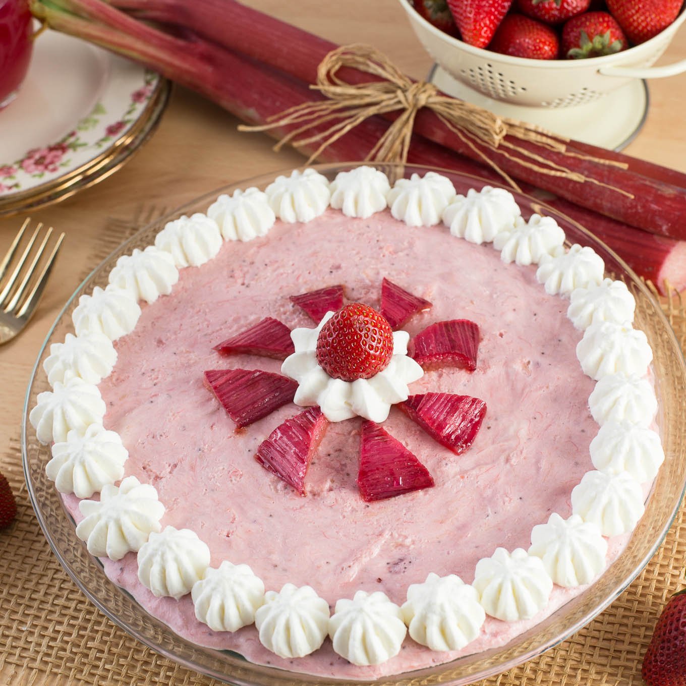 Mousse pie with strawberries and rhubarb, decorated with whipped cream dollops.