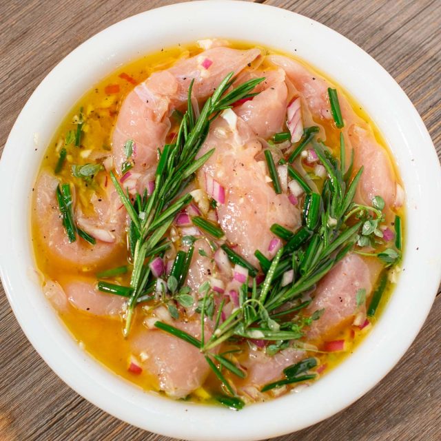 Chicken breasts in marinade of oil and rosemary sprigs.