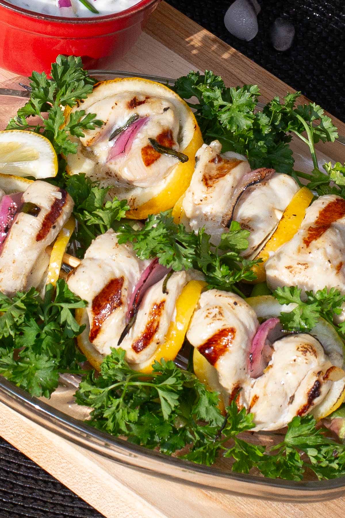 Two skewers of chicken, lemon slices and red onion kabobs on bed parsley.