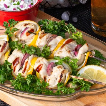 Two skewers of chicken, lemon slices and red onion kabobs on bed parsley.
