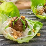 Lettuce leaf filled with rice noodles and topped with a meatball. Garnished with sliced green onions and chopped peanuts.