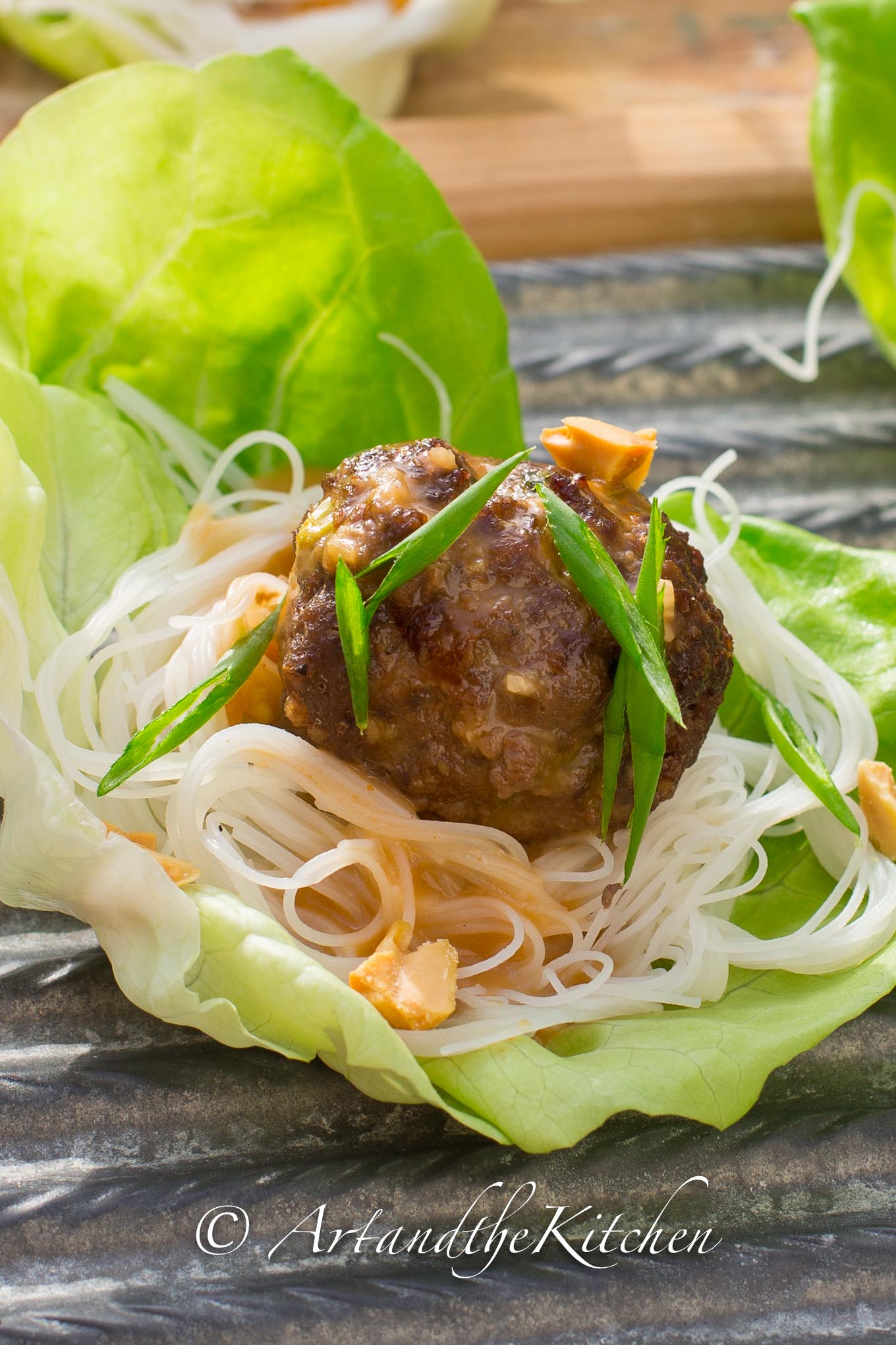 Lettuce leaf filled with rice noodles and topped with a meatball. Garnished with sliced green onions and chopped peanuts.