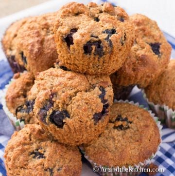 Bran muffins that are loaded with fresh blueberries on a blue gingham tablecloth.