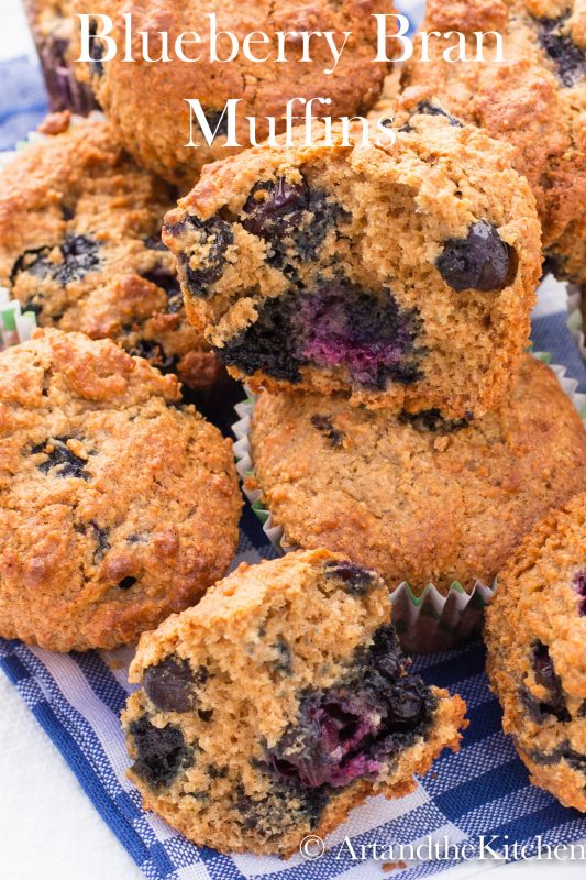 Bran muffins loaded with blueberries on gingham tablecloth.