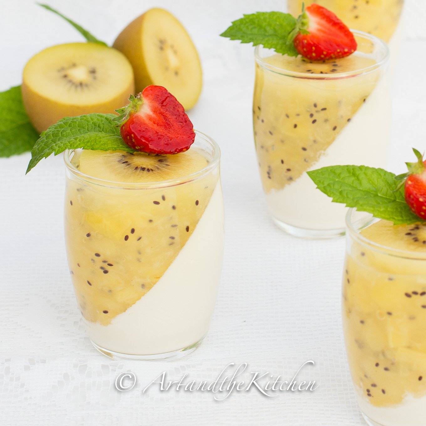 Glass jars filled with panna cotta and kiwi puree topped with mint and strawberry slice.