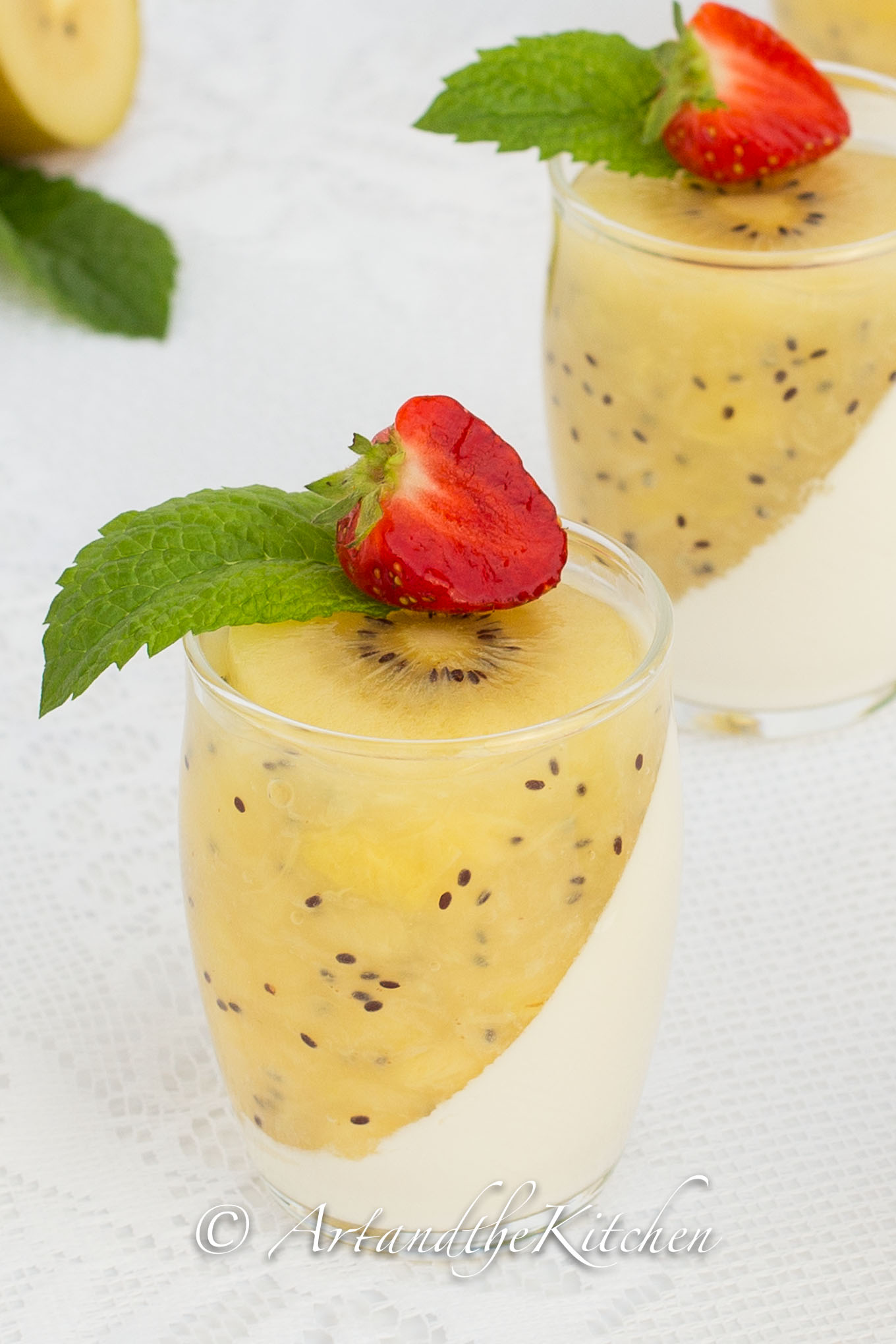 Glass jars filled with panna cotta and kiwi puree topped with mint and strawberry slice.