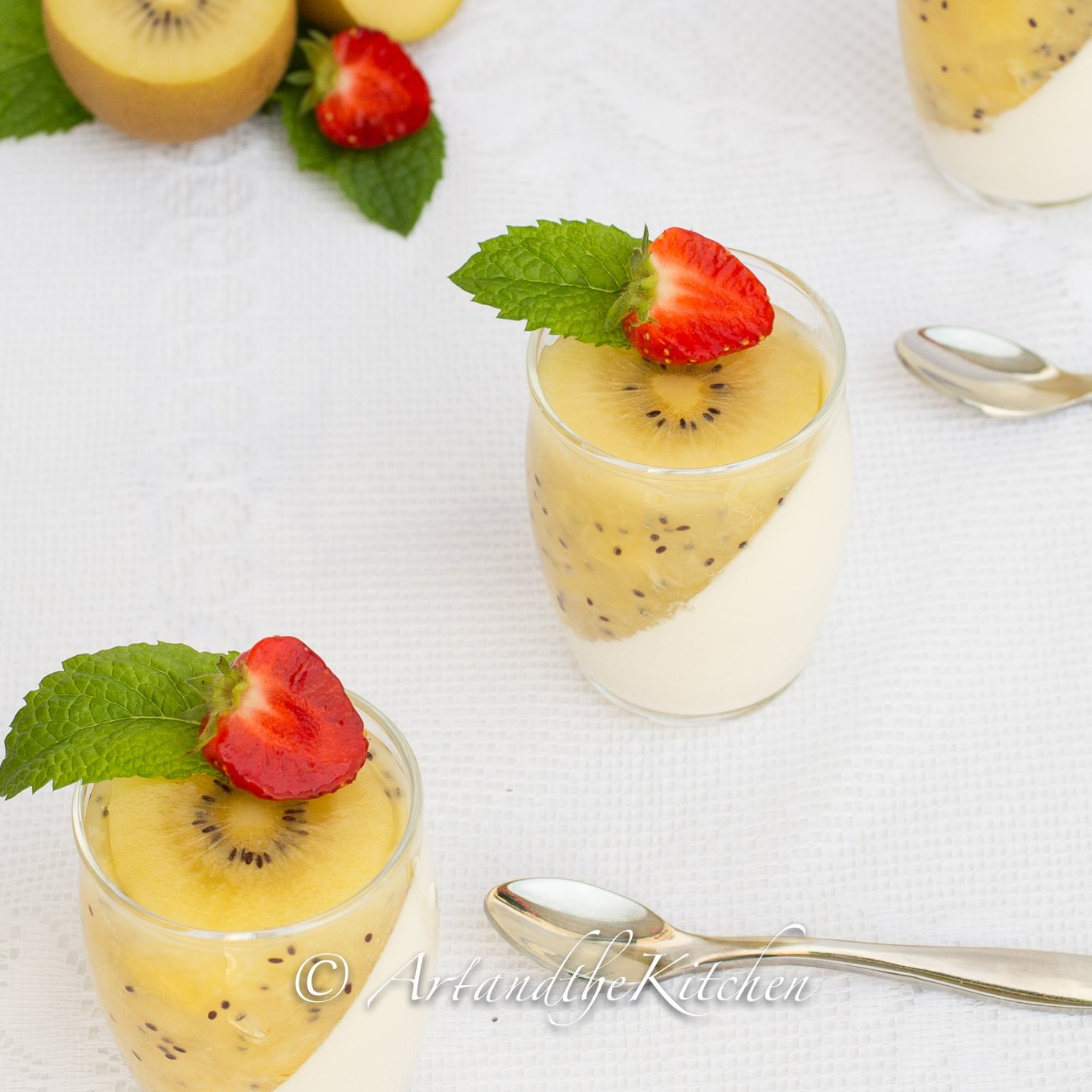 Glass jars filled with panna cotta and kiwi puree topped with mint and strawberry slice.