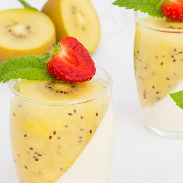 Glass jars filled with panna cotta and kiwi puree topped with mint and strawberry slice.