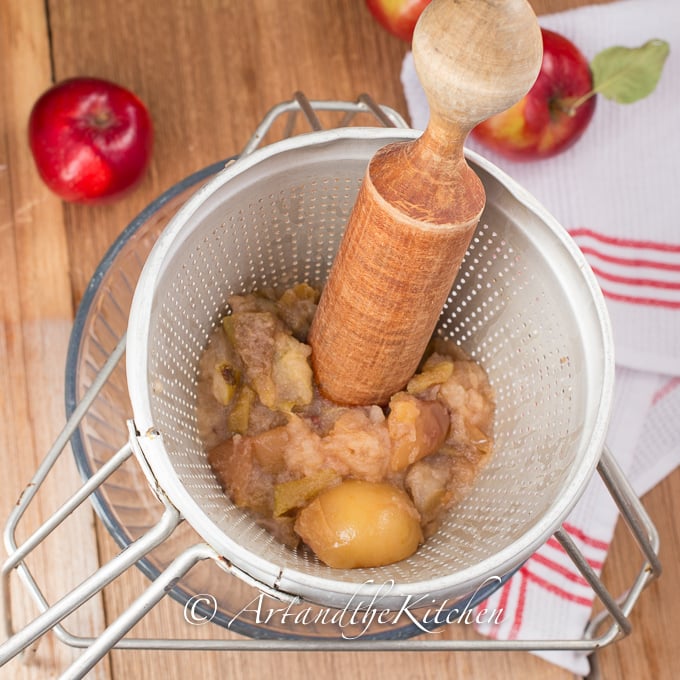 Cooked apples getting mashed in chinois strainer with wood pestle.