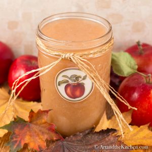 Glass jar with apple label on it, filled with applesauce. Jar has straw ribbon tied around it.