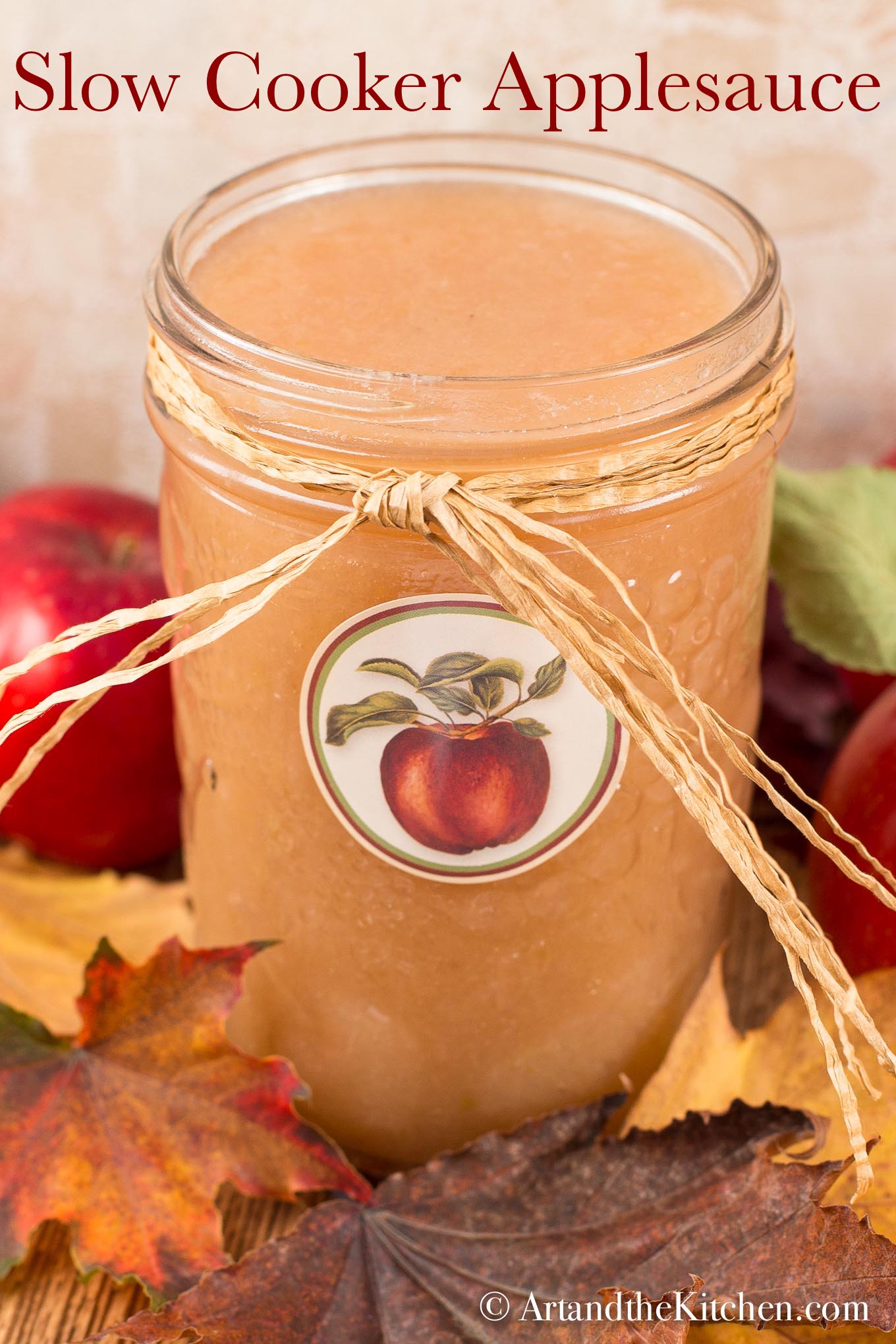 Glass jar with apple label on it, filled with applesauce. Jar has straw ribbon tied around it.