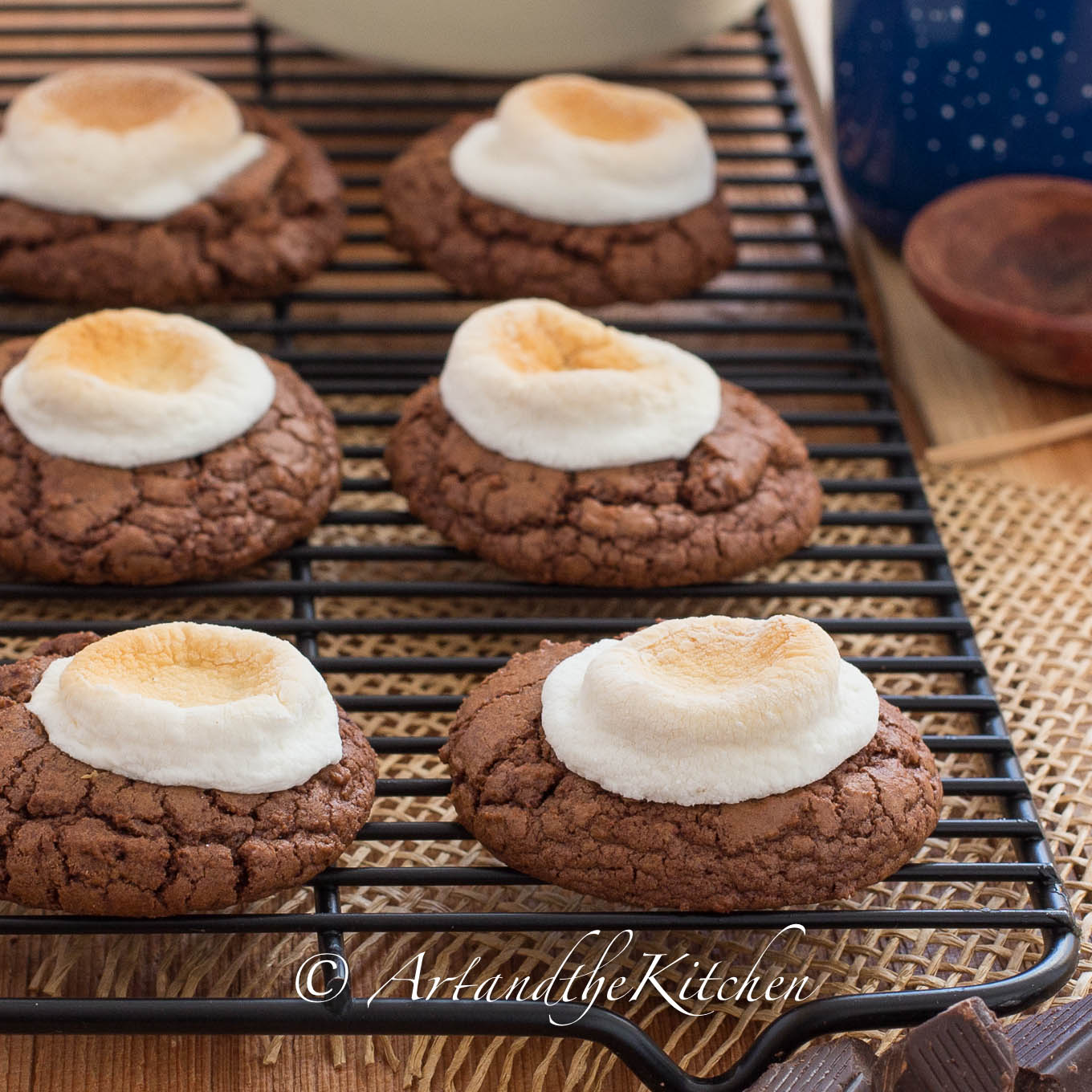 Chocolate cookies with toasted marshmallow on top on black baking rack.