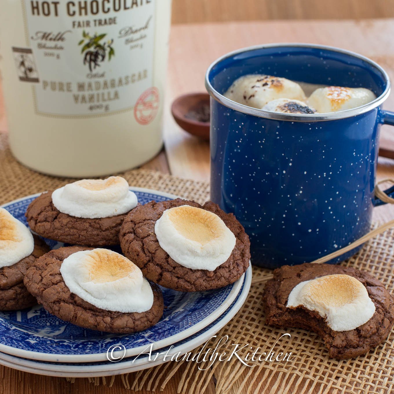 Chocolate cookies with toasted marshmallow on top blue plate with blue coffee mug of hot chocolate.